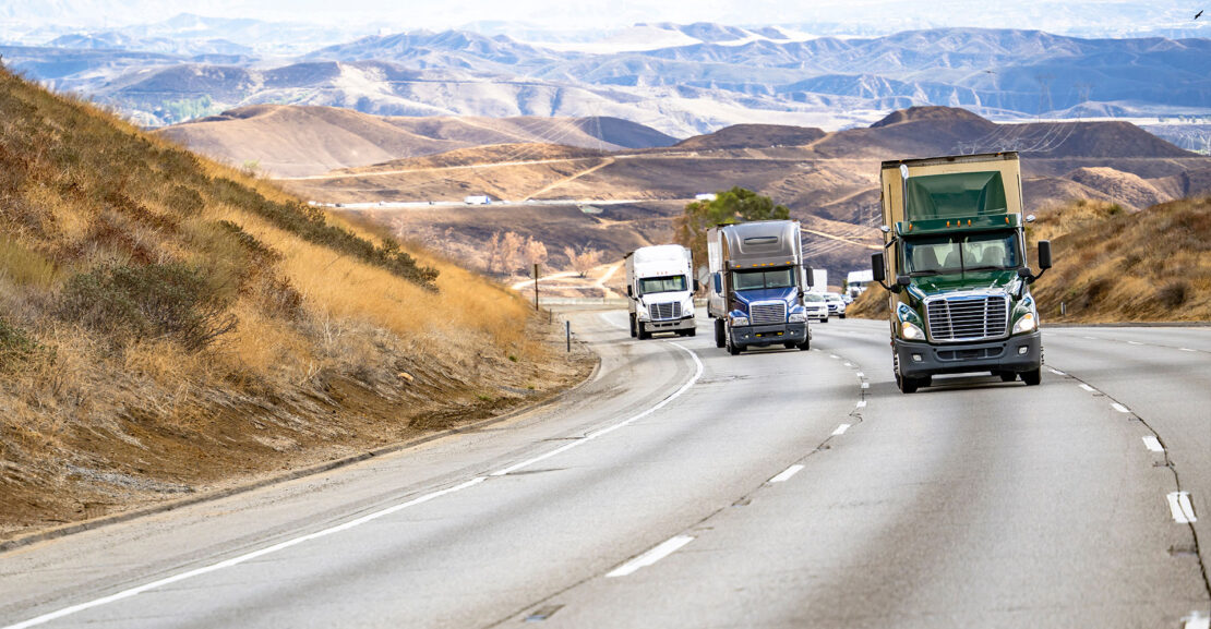 Row of semi trucks driving down highway in southern California
