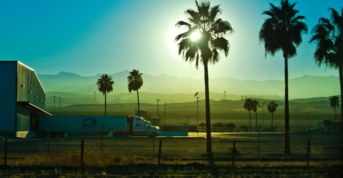 Semi-tractor trailer truck unloading with palms in a sunset california landscape