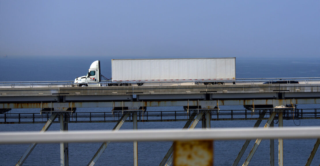 White semi truck crossing long bridge near ports.