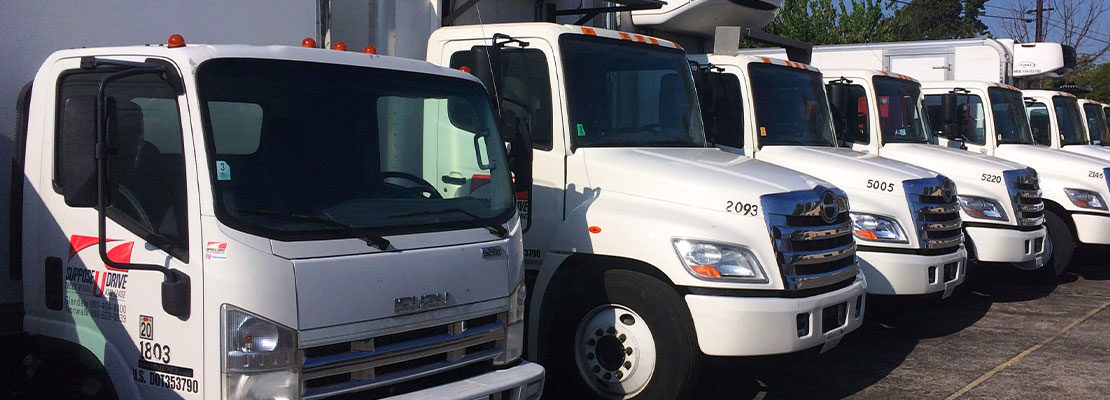 How-Truck-Rentals-and-Leases-Save-You-More-Than-Just-Money-SUpposeUDrive Row of white Suppose U Drive commercial trucks, in a variety of types and styles.