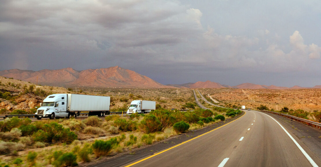 Semi trucks on an Arizona highway with mountains in background and blue sky with fluffy clouds