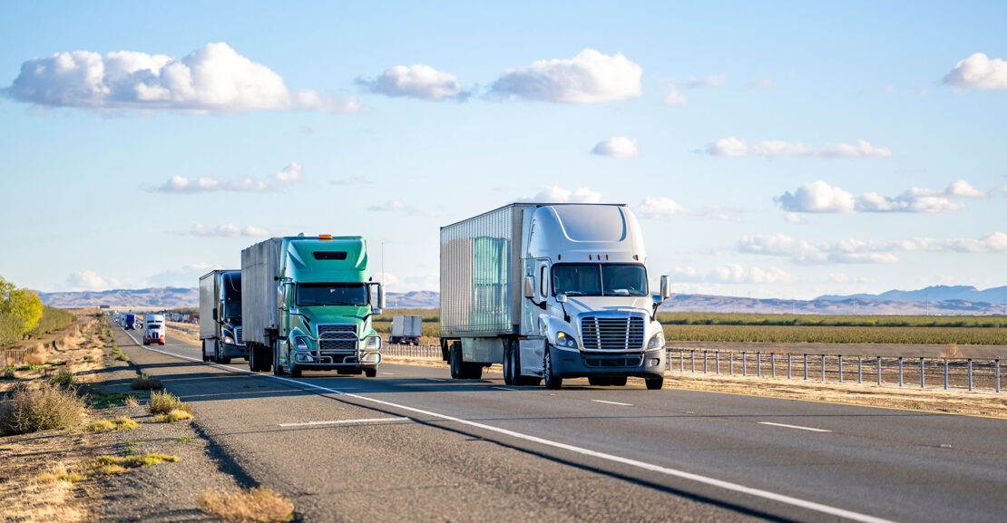 Convoy of the big rig semi trucks with different semi trailers carry cargo running on the divided highway road in both directions