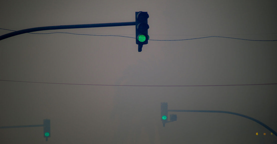 Green traffic lights hanging overhead in intense fog