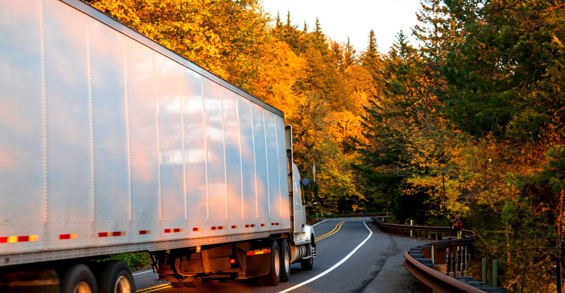 Big rig semi truck transporting cargo in dry van semi trailer driving on winding autumn colored road