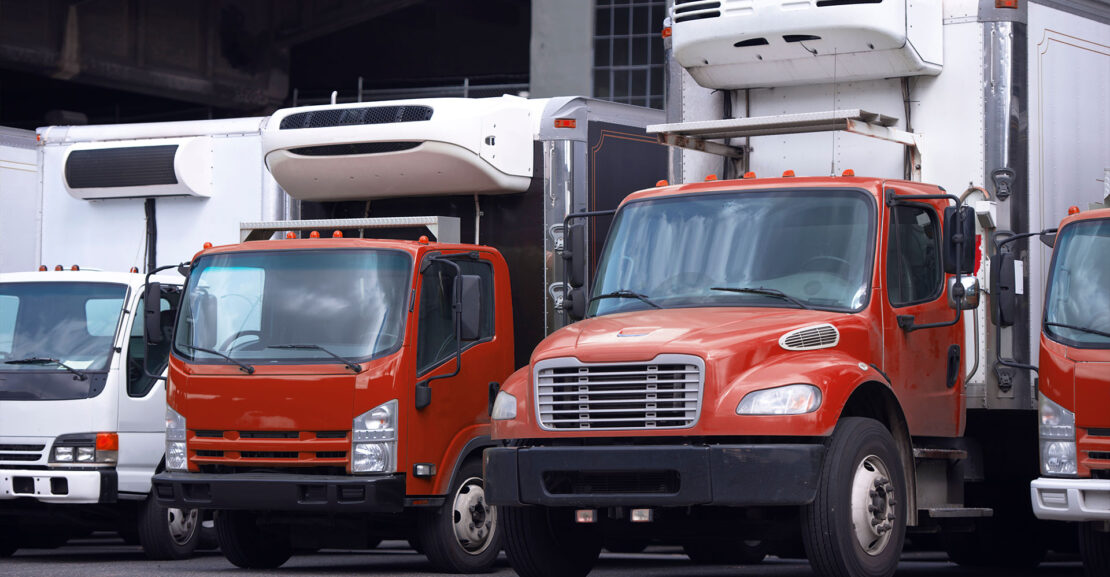 Small size local semi trucks with box refrigerator trailer stand in row in warehouse dock