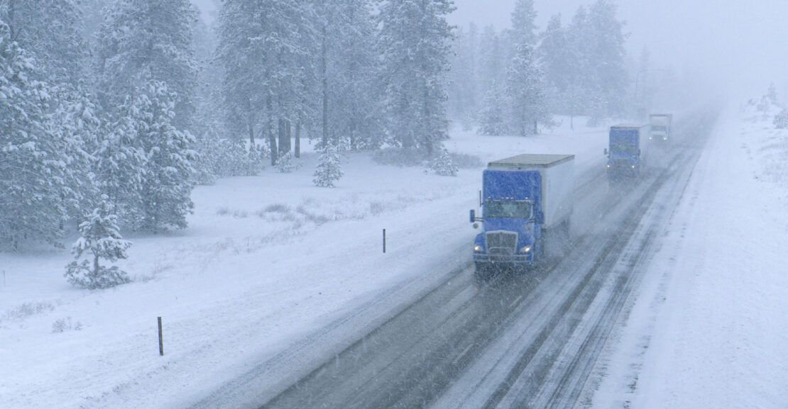Trucks haul containers down an expressway and through a snowstorm.